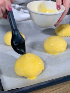 Teigkugeln fuer die Osterpinzen mit verquirltem Ei bestreichen