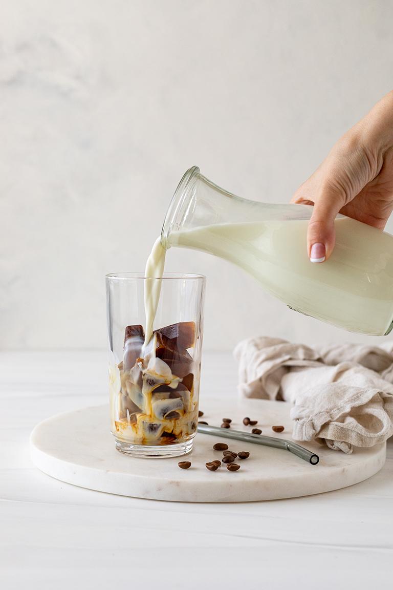 kalte Milch wird auf die Kaffee Eiswuerfel im Glas gegossen um einen leckeren Eiskaffee nach einem Rezept von Sweets & Lifestyle® zu erhalten
