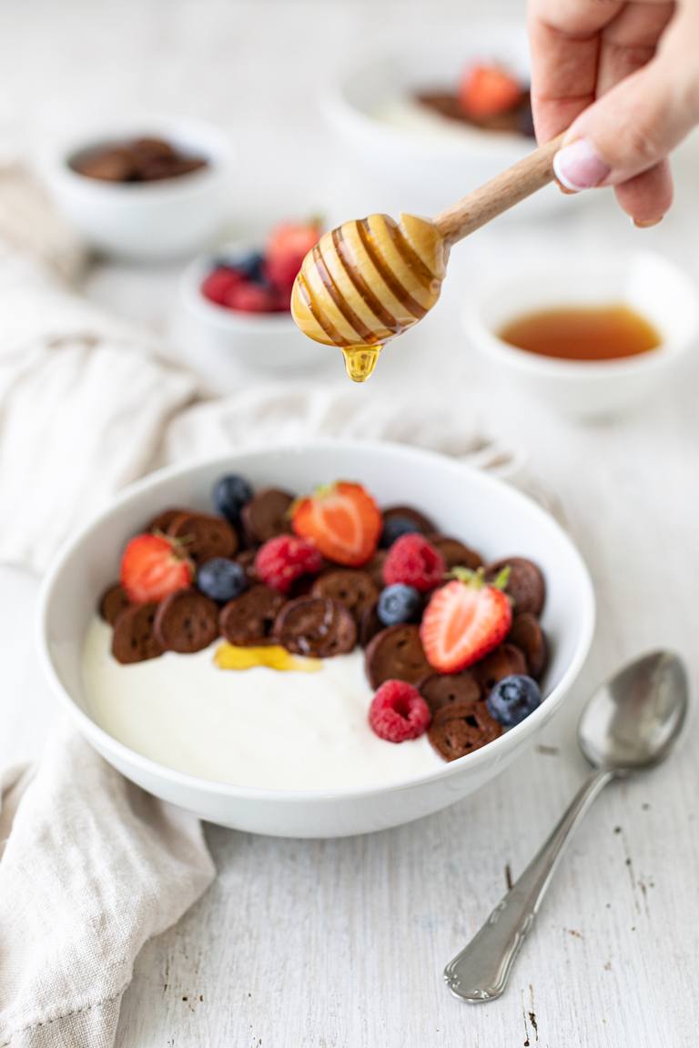 Frischer Honig wird zum Suessen der Pancake Cereal mit Kakao und frischen verwendet