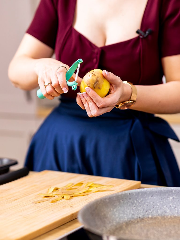 Foodbloggerin und Kochstudio Inhaberin Verena Pelikan beim Schaelen einer rohen Kartoffel fuer ihre Kartoffelgratin Roeschen