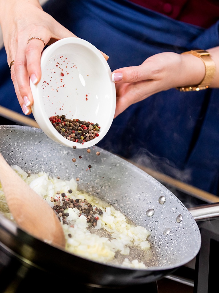 Foodbloggerin Verena Pelikan gibt Pfefferkoerner zu den Zwiebelstuecken in der aufgeschaeumten Butter fuer ihre Pfeffersauce