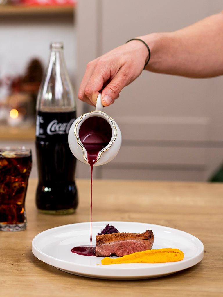 TV Koch Alexander Kumptner giesst Orangen Rotwein Sauce zur gebratenen Entenbrust mit Kuerbispueree und Rotkraut auf das Teller