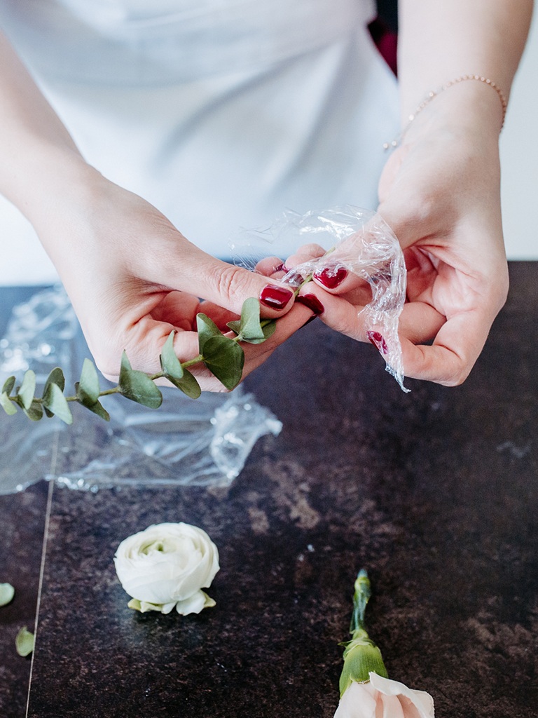 Stiele vom Eukalyptus und Blumen werden mit Frischhaltefolie umwickelt um in einen Strohhalm gegeben und in eine Hochzeitstorte gesteckt zu werden