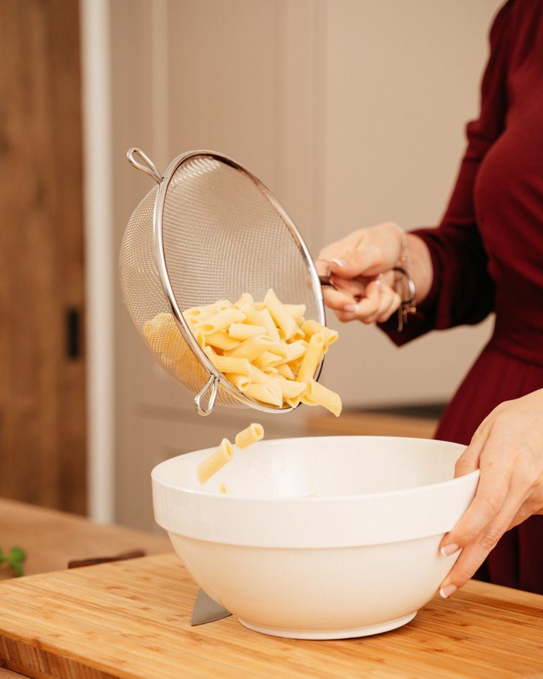 Gekochte Penne Nudeln werden von Foodbloggerin Verena Pelikan fuer ihren italienischen Nudelsalat in eine Salatschuessel gegeben