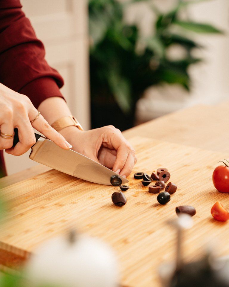 Foodbloggerin Verena Pelikan beim Schneiden von schwarzen Oliven fuer ihren mediterranen Nudelsalat mit Tomaten, Rucola und Mozzarella