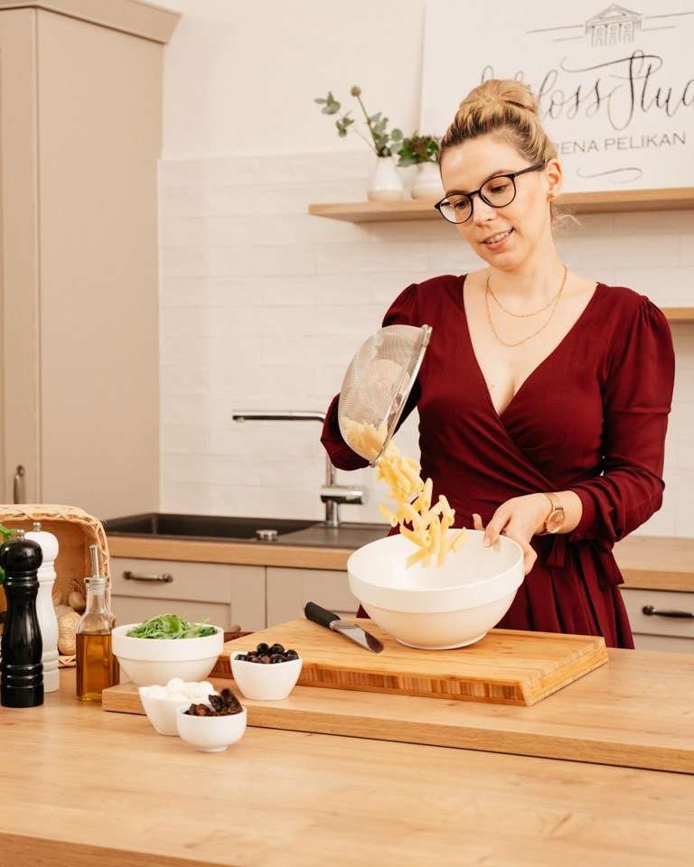 Foodbloggerin Verena Pelikan leert gekochte abgeseihte Nudeln in eine Salatschuessel fuer ihren italienischen Nudelsalat