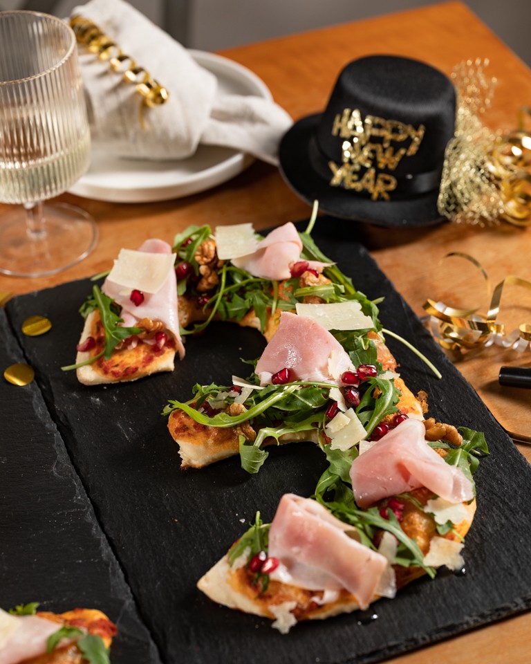 Pizza in Form einer Jahreszahl belegt mit Rucola Schinken Granatapfelkernen und Walnuessen als pikantes Fingerfood fuer die Neujahrsparty