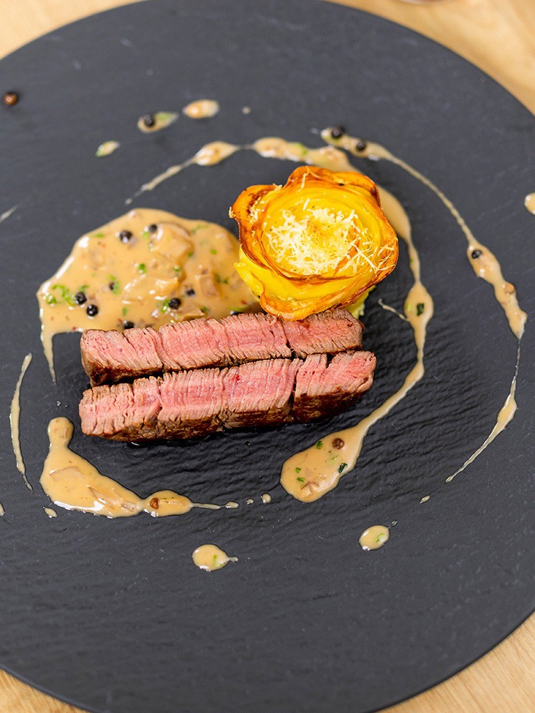 Steak-mit-Pfeffersauce-und-Kartoffelgratin-Roeschen-auf-schwarzem-Teller-angerichtet-als-Festtagsgericht