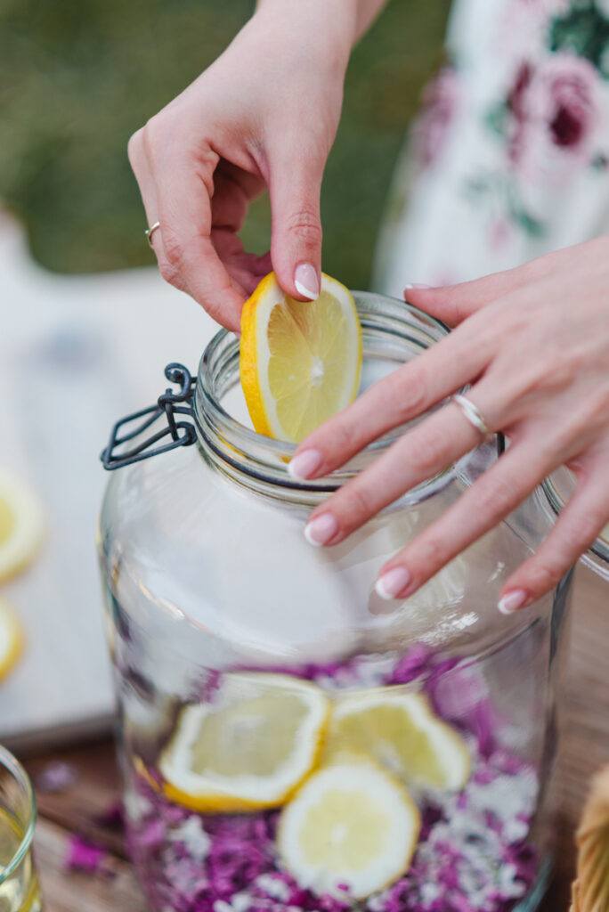 Zitronenscheiben kommen zu den Fliederblueten in das Glas fuer die Herstellung von selbst gemachten Fliederbluetensirup