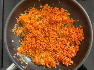 Rote Linsen kommen fuer die Linsenbratlinge zu den angeschwitzten Zwiebelwuerfel und geraspelten Karotten in die Pfanne