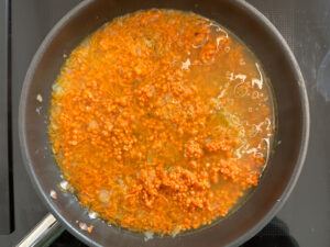 Suppe in der Pfanne mit den geduensteten Zwiebeln Karotten und Linsen fuer die Zubereitung der Linsenbratlinge